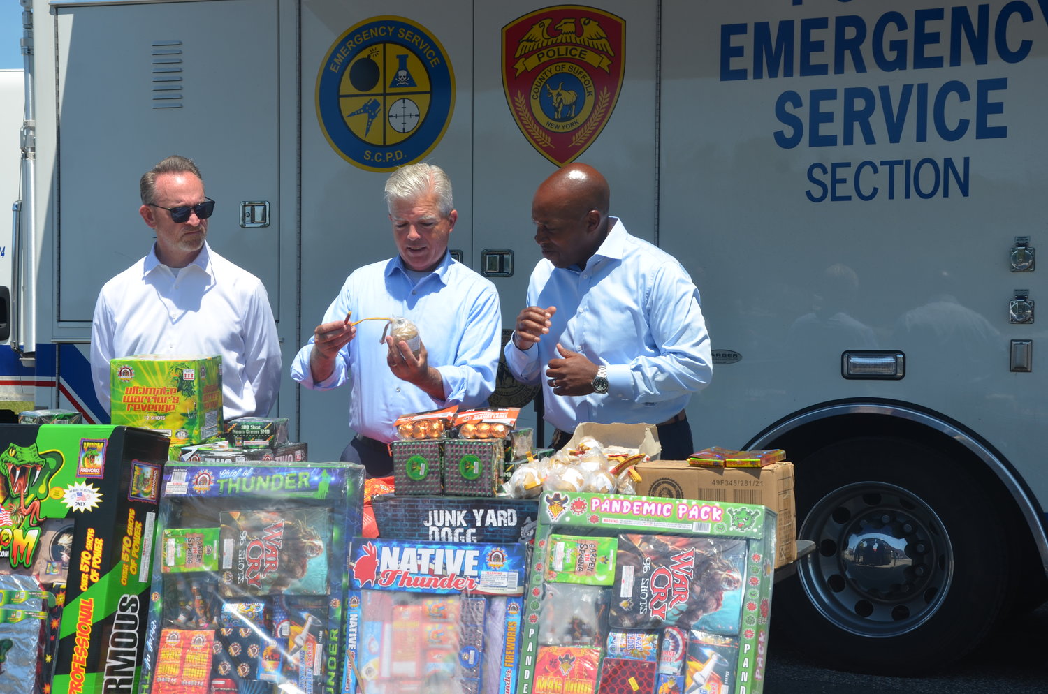 (From L to R) Suffolk County Fire, Rescue, and Emergency Services Commissioner Pat Beckley, Suffolk County Executive Steve Bellone and Suffolk County Police Commissioner Rodney K. Harrison look through a table full of illegal fireworks seized by the SCPD.